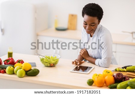 Black Woman Using Digital Tablet Cooking Browsing Healthy Recipes Online Preparing Dinner In Modern Kitchen At Home. Online Cooking Courses. Weight Loss Application Advertisement Concept