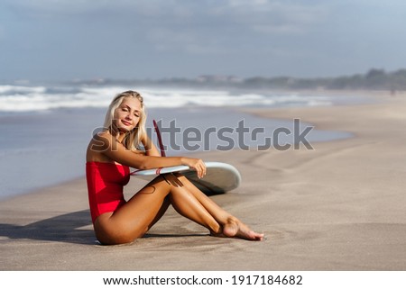 Surf woman with long blonde hair go to ocean. Female holding surfboard ready to surf. Bali island, Indonesia. Outdoor Active Lifestyle.