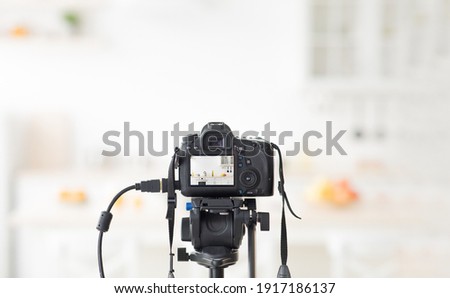 Stylish kitchen with minimalist interior for sale or rent of house or flat. Professional camera takes photo of blurred room, plate with bright apples, utensils on furniture, white walls, in daylight