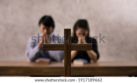 A young Asian Christian couple praying to Jesus Christ in a church.