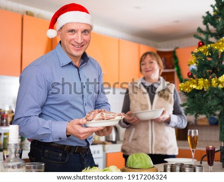 Man with plate of meat during cooking for xmas dinner, senior woman behind