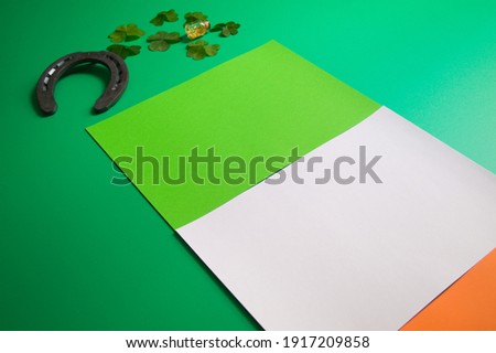 lucky horseshoe with group of three-leaf covers and pot of liquid gold on green background and flag of ireland