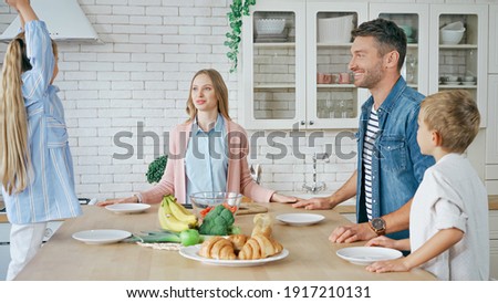 Positive family looking at girl near fresh food and pastry in kitchen