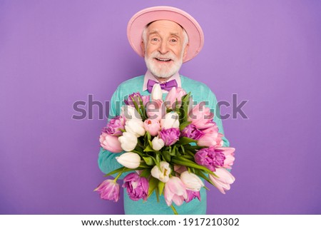 Portrait of satisfied aged person hands hold flowers beaming smile look camera isolated on purple color background Royalty-Free Stock Photo #1917210302