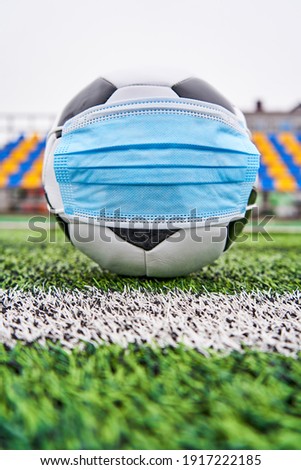 Soccer ball in empty stadium. Football Ball in medical mask to protect against coronavirus, against background of plastic seats without people. Vertical photo           