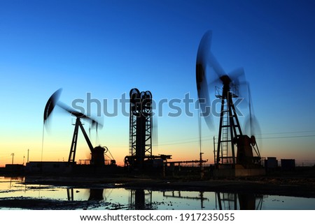 Oil field site, in the evening, oil pumps are running, Silhouette of beam pumping unit