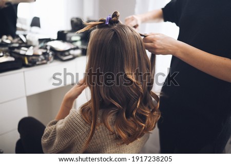 Hair stylist prepares woman makes curls hairstyle with curling iron. Long light brown natural hair Royalty-Free Stock Photo #1917238205