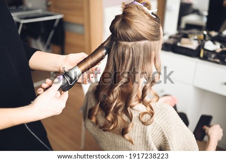 Hair stylist prepares woman makes curls hairstyle with curling iron. Long light brown natural hair Royalty-Free Stock Photo #1917238223