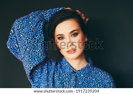 Fashion portrait of stylish young brunette woman wearing blue animal pring clothes, posing on black background
