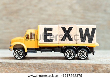 Toy truck hold alphabet letter block in word EXW (abbreviation of Ex works) on wood background