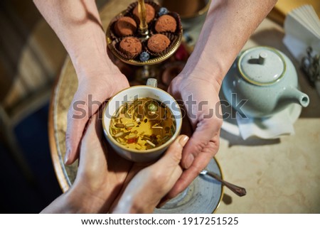 Cropped photo of two pairs of hands holding a cup of freshly-made herbal tea