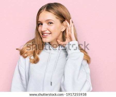 Beautiful young caucasian girl wearing casual sweatshirt smiling with hand over ear listening an hearing to rumor or gossip. deafness concept. 