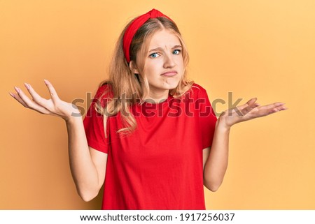 Beautiful young caucasian girl wearing casual red t shirt clueless and confused with open arms, no idea and doubtful face. 