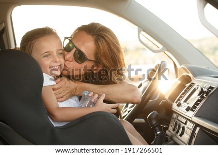 Woman behind the wheel with white t-shirt in holiday context kisses her daughter with smiling expressions
