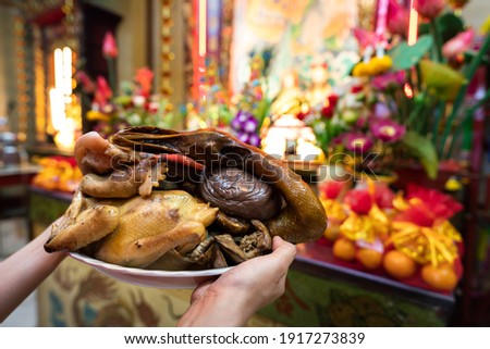 Action of paying respect to Chinese god during Chinese new year ceremony with various type of meats and foods. Close-up and selective at food (chicken) part in the tray on people's hand. Royalty-Free Stock Photo #1917273839