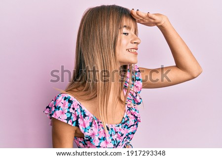 Teenager caucasian girl wearing casual clothes very happy and smiling looking far away with hand over head. searching concept. 