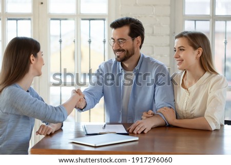 Happy young married family couple shaking hands with real estate agent, getting acquainted at meeting, celebrating making agreement or thanking for high quality professional service in office. Royalty-Free Stock Photo #1917296060