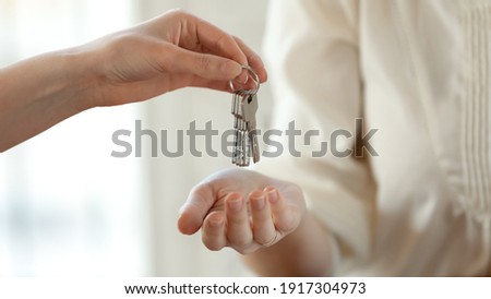 Close up young female real estate agent giving keys to happy buyer, congratulating with purchasing apartment. Millennial woman taking in leasing new house, accommodation tenancy rental service concept Royalty-Free Stock Photo #1917304973