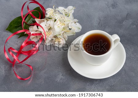 White cup with coffee on a gray background. A bouquet of orchids entwined with a ribbon in the background. Banners, congratulations on the holiday. Copy space.