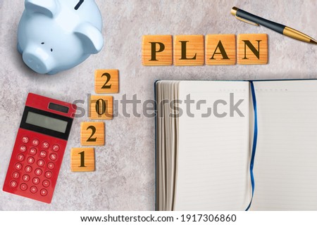 2021 plan concept with blank notebook, piggy bank, calculator and wooden block.