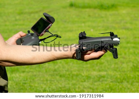 Man with remote control cell phone hold drone. Sunny green nature background.