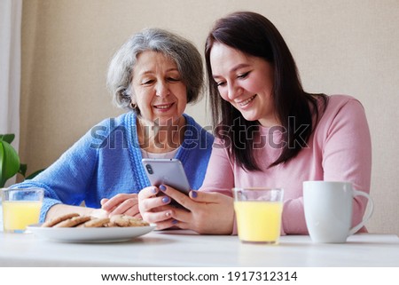 Happy two generations of family an elderly mother and a young daughter are having fun using a mobile phone to view content on the Internet - Women are having fun using wi-fi and a smartphone Royalty-Free Stock Photo #1917312314
