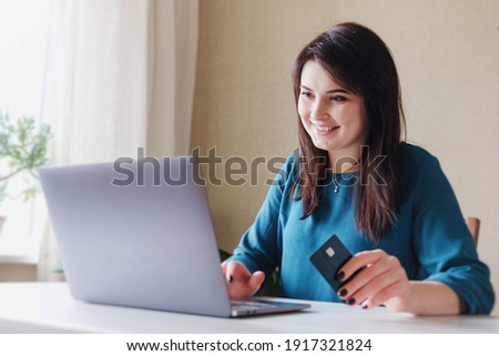 Girl holding a debit card and shopping online with a laptop - Young smiling millennial girl shopping on the Internet - Girl pays bills by credit card for online payments