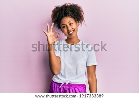 Beautiful african american woman with afro hair wearing sportswear smiling positive doing ok sign with hand and fingers. successful expression. 