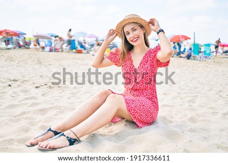 Young blonde woman on vacation smiling happy sitting on the sand at the beach