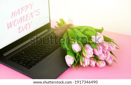 A bunch of pink tulips near a laptop with HAPPY WOMEN'S DAY signature. 8 march