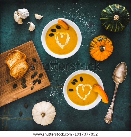 Pumpkin soup with cream and pumpkin seeds on dark green background, decorated with little pumpkins and garlic, top view