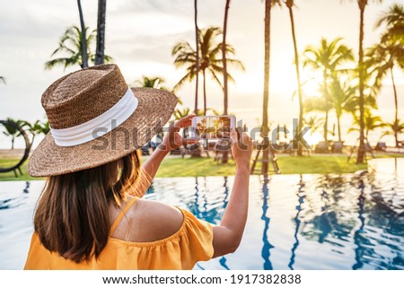 Young woman traveler taking a beautiful sunset  at tropical resort beach, Travel lifestyle concept