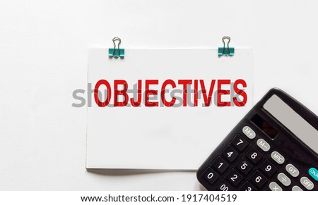 On a white background lies a calculator and a notebook with the word objectives