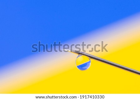 Needle top of syringe with a drop in front of Ukrainian flag. Ukrainian flag reflects in the drop on the needle, vaccination in Ukraine