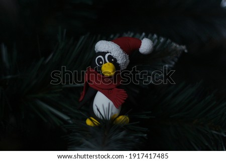 hand made penguin in a santa claus  hat with pompon and red scarf sits on branch of the christmas tree and stares intently