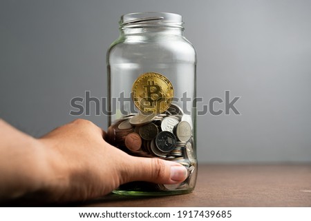 Golden bitcoins with piles of cents coins inside a glass jar with a men hand grab the jar