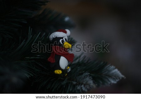 holiday penguin in a santa claus  hat with pompon and red scarf sits on branch of the christmas tree and looks sideways