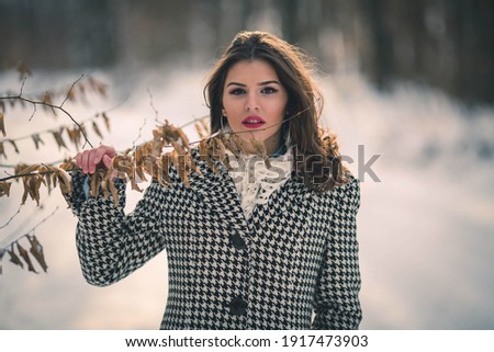 A shallow focus shot of a female wearing a fashionable coat while holding on a tree in a winter forest