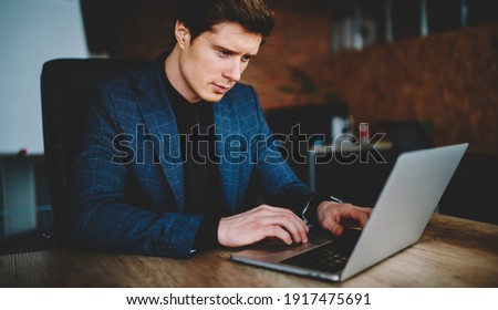 Confident corporate employer using laptop computer during working time in office interior, Caucasian businessman reading financial publication browsed on modern netbook technology with 4g internet