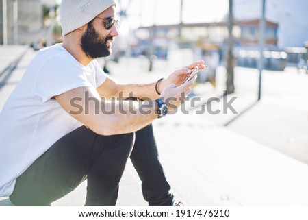 Middle Eastern male tourist with nicotine cigarette in hand browsing website with online tips to get rid of bad habits, Turkish smoker in sunglasses reading received email message and writing text