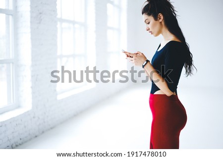 Caucasian generation Z with brunette hair using mobile technology for online messaging and networking during leisure browsing, millennial female trainer checking sportive results on smartphone device
