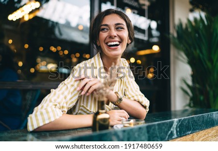 Cheerful young ethnic female in trendy outfit laughing and looking away while chilling at marble counter on cozy cafe terrace