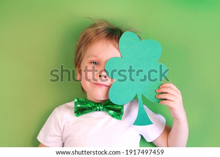 Cute smiling сhild boy holding paper clover shamrock on green background. Irish St. Patrick's Day.