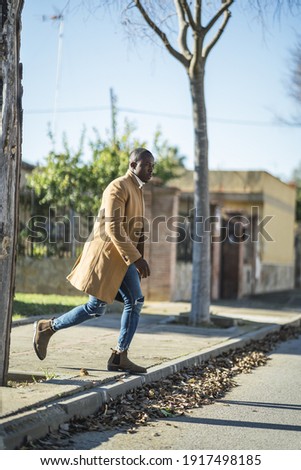 A shallow focus shot of a stylish handsome African male in a coat crossing the road