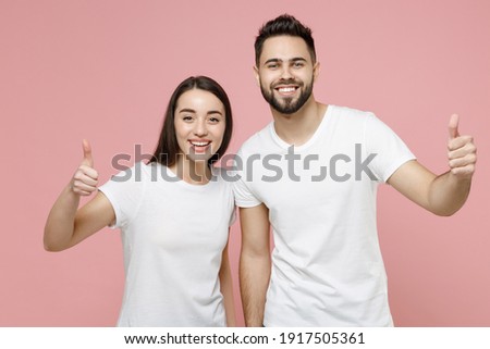 Young cheerful couple two friends bearded man brunette woman in white basic blank print design t-shirts smiling showing thumbs up like gesture isolated on pastel pink color background studio portrait Royalty-Free Stock Photo #1917505361