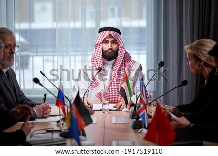 Arabic sheikh man presenting his ideas to diverse multi-ethnic colleagues and listening for ideas for success investments at bright modern office room, use microphone. meeting without ties