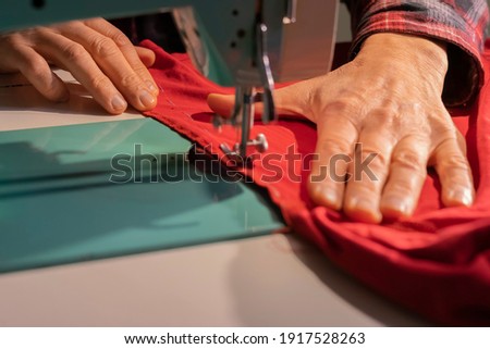 Tailor at work on an old sewing machine, red cloth, makes a seam