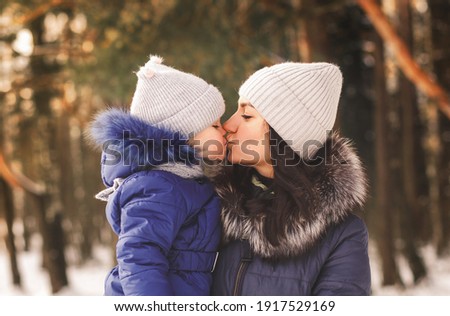 Mom kisses a little girl on a walk in the woods in winter. Motherly love
