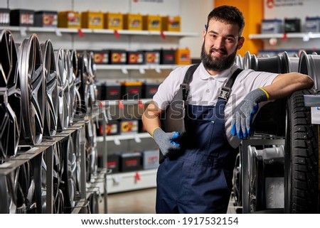 adult auto mechanic man in uniform have rest after hard working day, standing by rack of car wheels. auto, car, transport concept Royalty-Free Stock Photo #1917532154