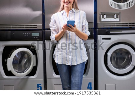Laundry, smiling woman holding phone, washing clothes via app. Cropped young caucasian female is ready to wash clothes Royalty-Free Stock Photo #1917535361